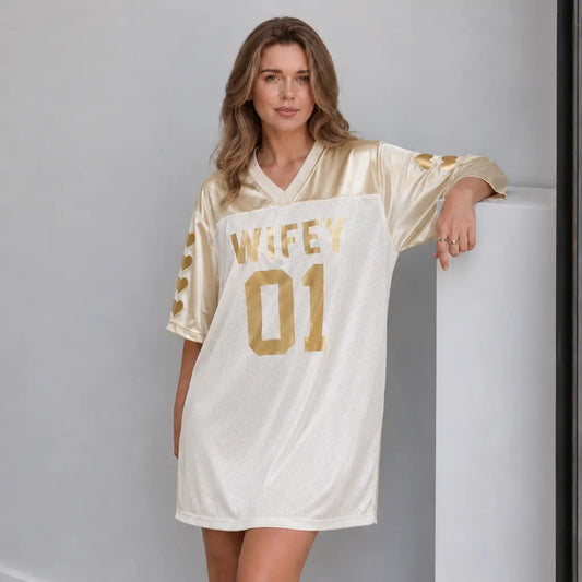 Woman wearing a gold and white 'WIFEY 01' jersey against a gray background