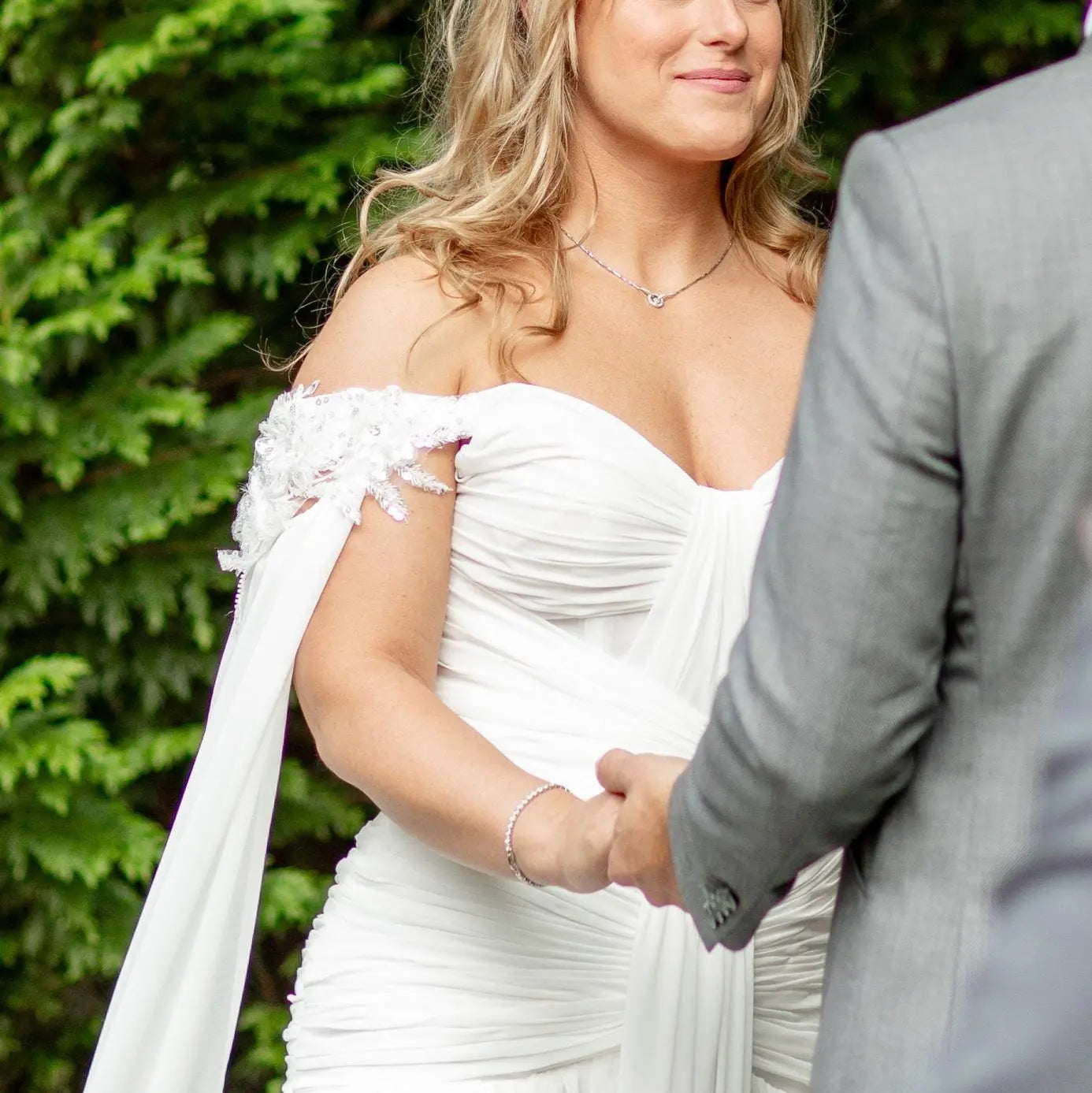 Woman in a white wedding dress standing outdoors with greenery in the background